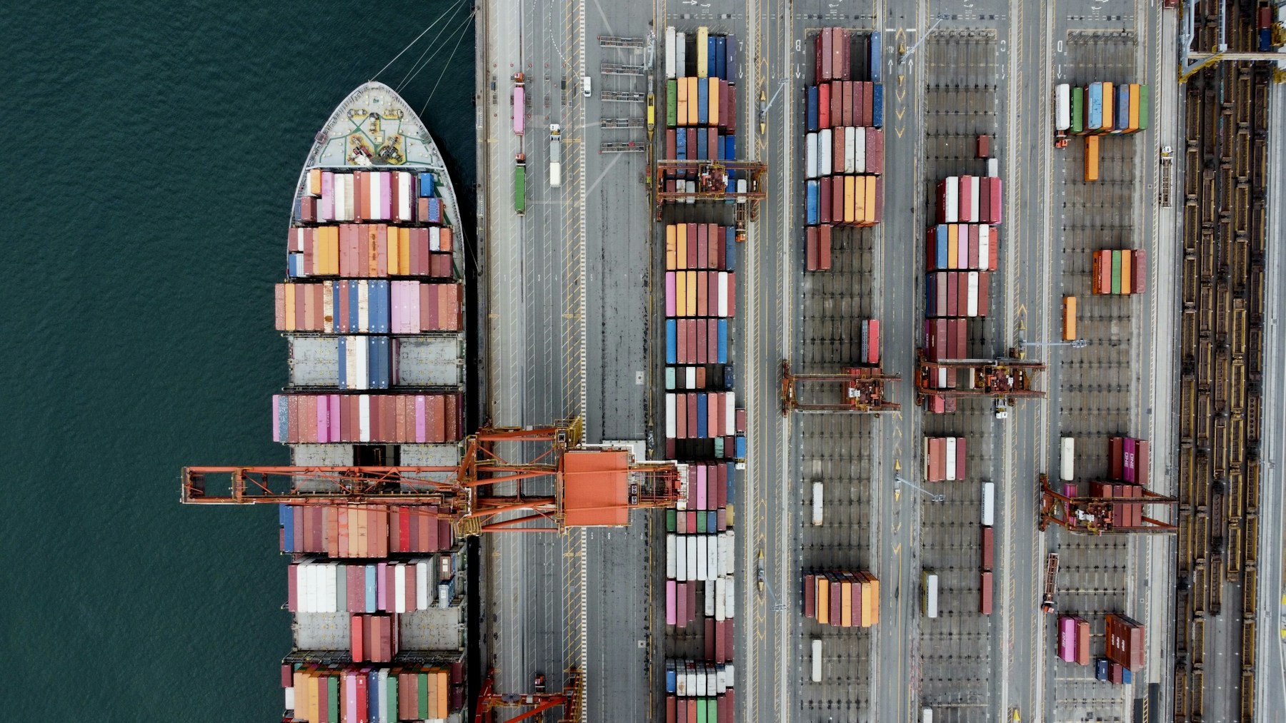 Container ship alongside port cranes and rows of cargo containers